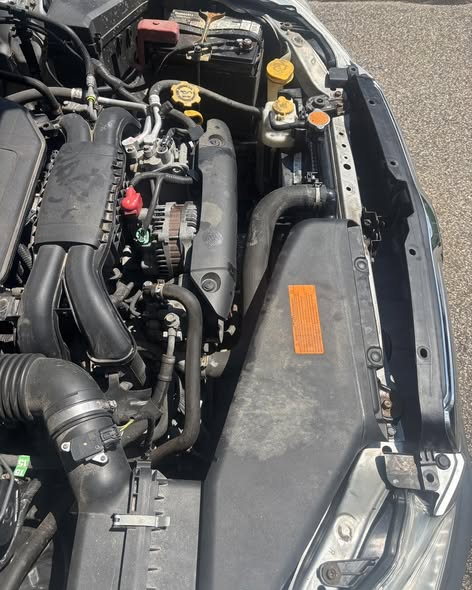An open engine bay seen from above, with the air intake, alternator, coolant hoses and reservoir visible alongside the front support panel.