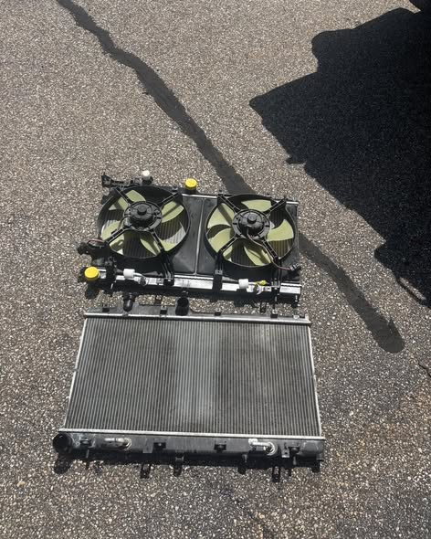 A radiator with its twin electric cooling fan shroud, removed from a vehicle and laid out on sunlit asphalt.